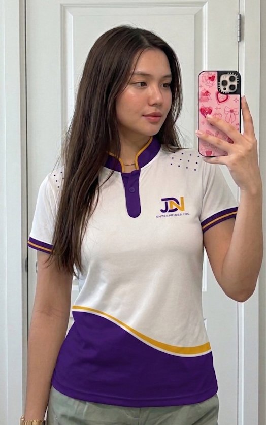 Team member taking a mirror photo in the JDN employee polo: white Chinese collar polo with purple wave, gold trim and JDN logo